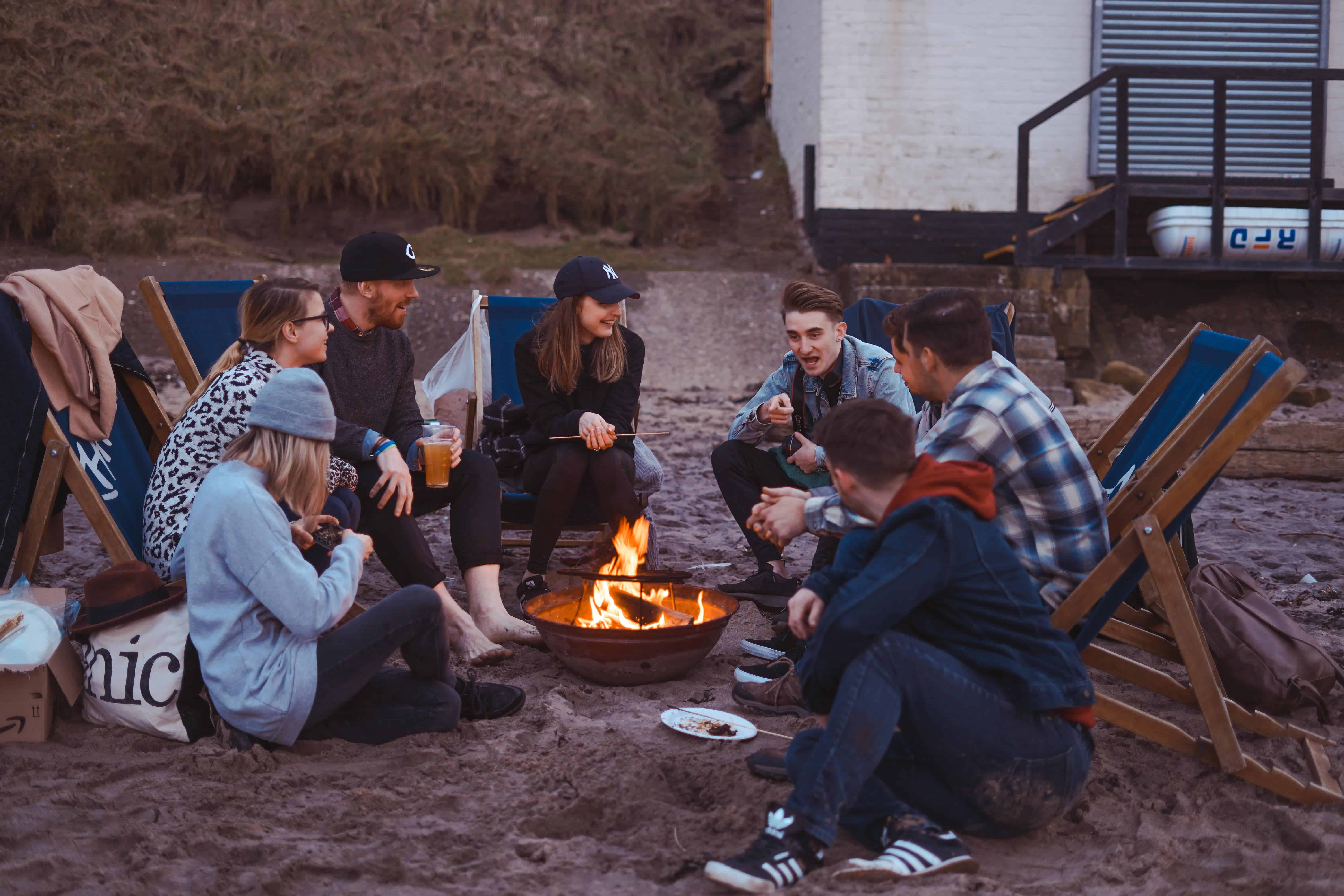 Group of teens and young adults sitting around a camp fire.