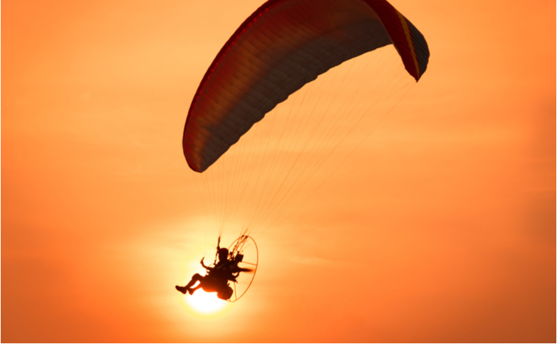 Silhouette of a paramotor control flying through soft sunlight sunset sky.