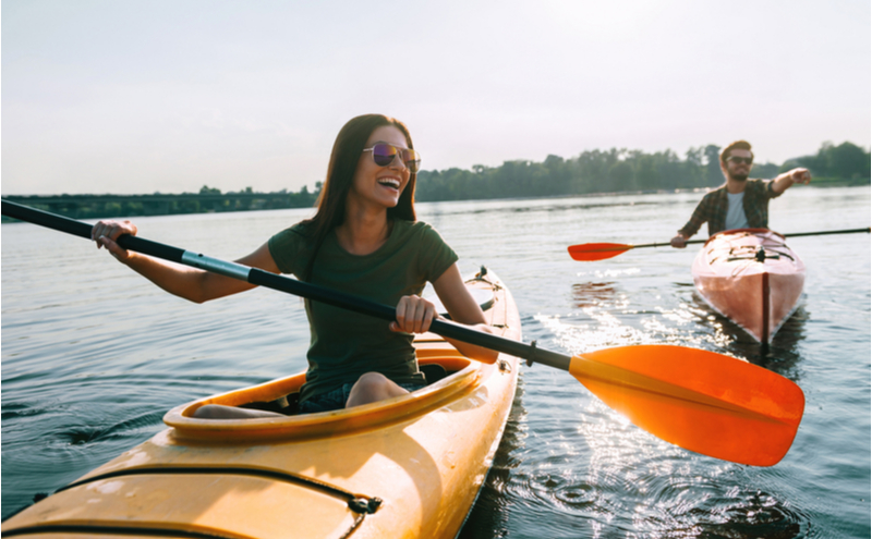 young couple kayaking on lake together and smiling.