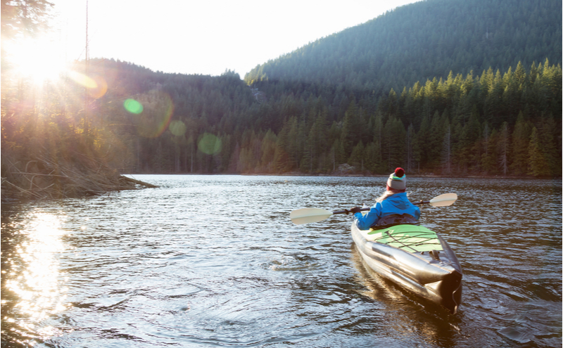 Adventurous girl is kayaking on an inflatable kayak in a beautiful natural lake.