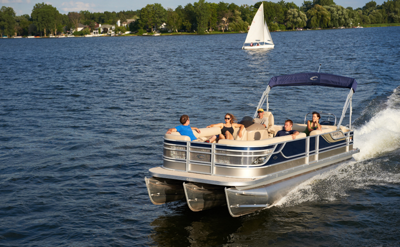 Group of people driving a pontoon boat on a lake.