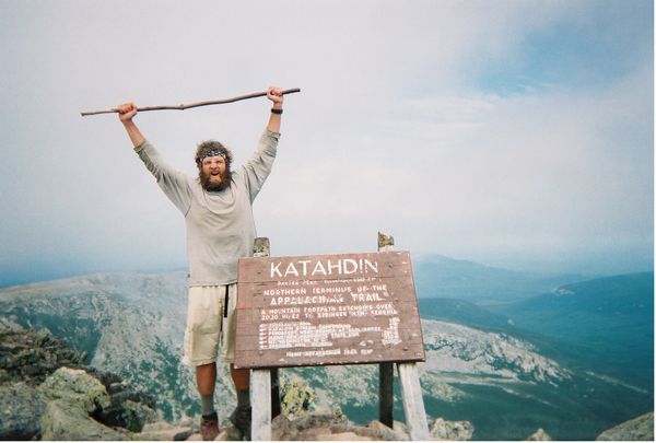 Hiker at the top of mount Katahdin by the sign.