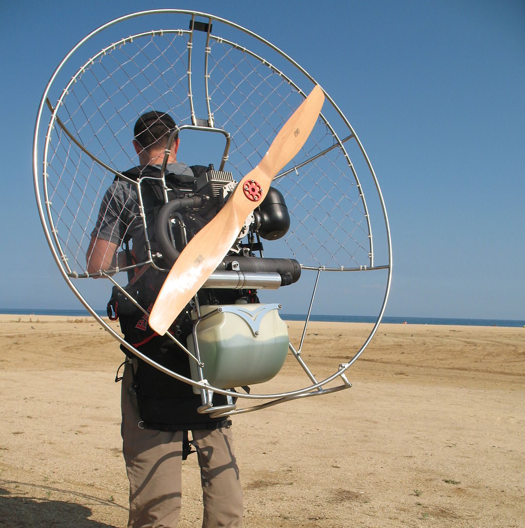 Man standing in desert with paramotor on back.