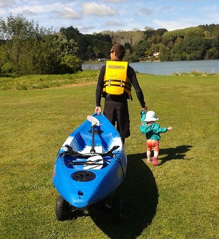 Dad holding hands with baby pulling kayak on a cart.
